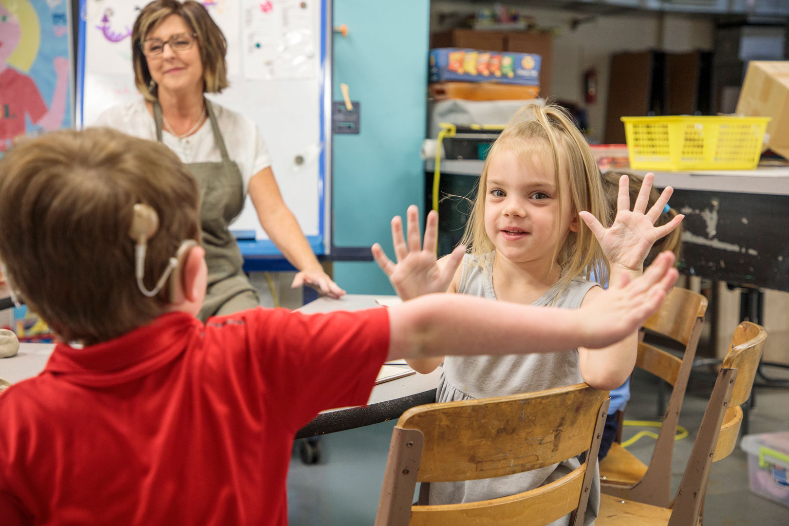 Two preschoolers sitting at a table giving high fives.