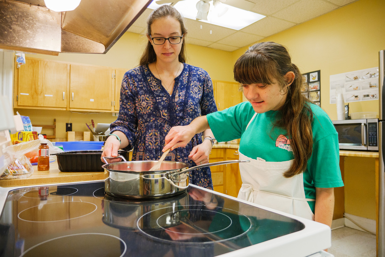 A teen learning how to use a stove for cooking with a parent.