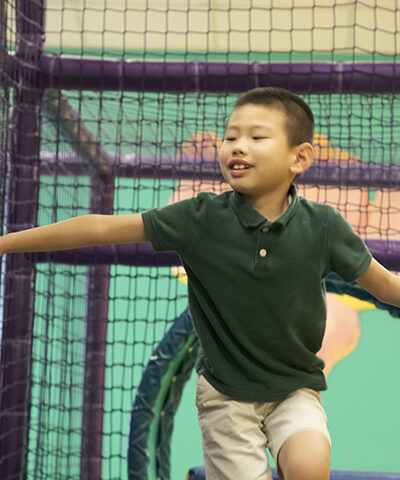 A boy walking through an indoor obstacle course. His arms are out.
