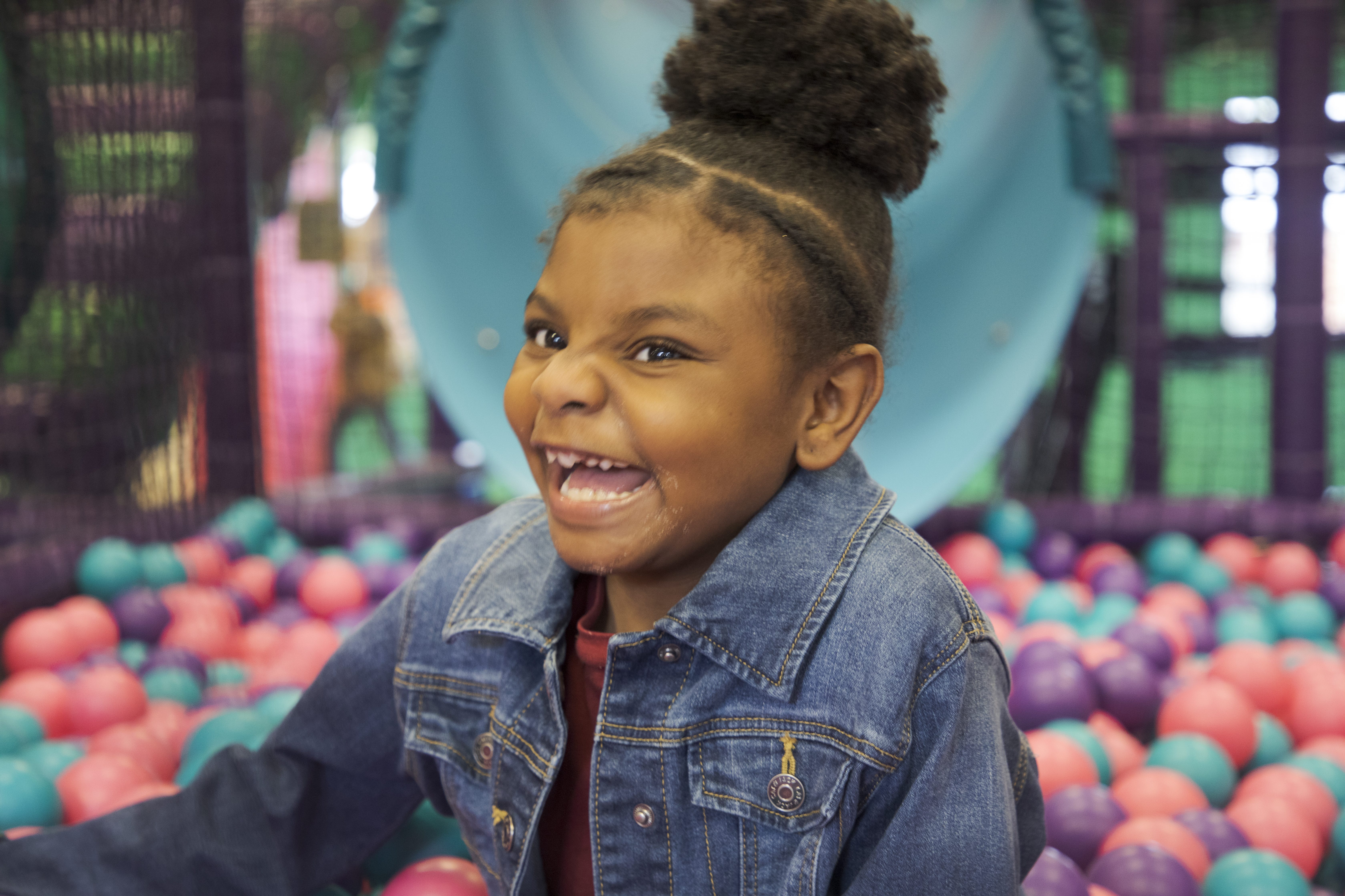 A girl in a ball pit smiling big.
