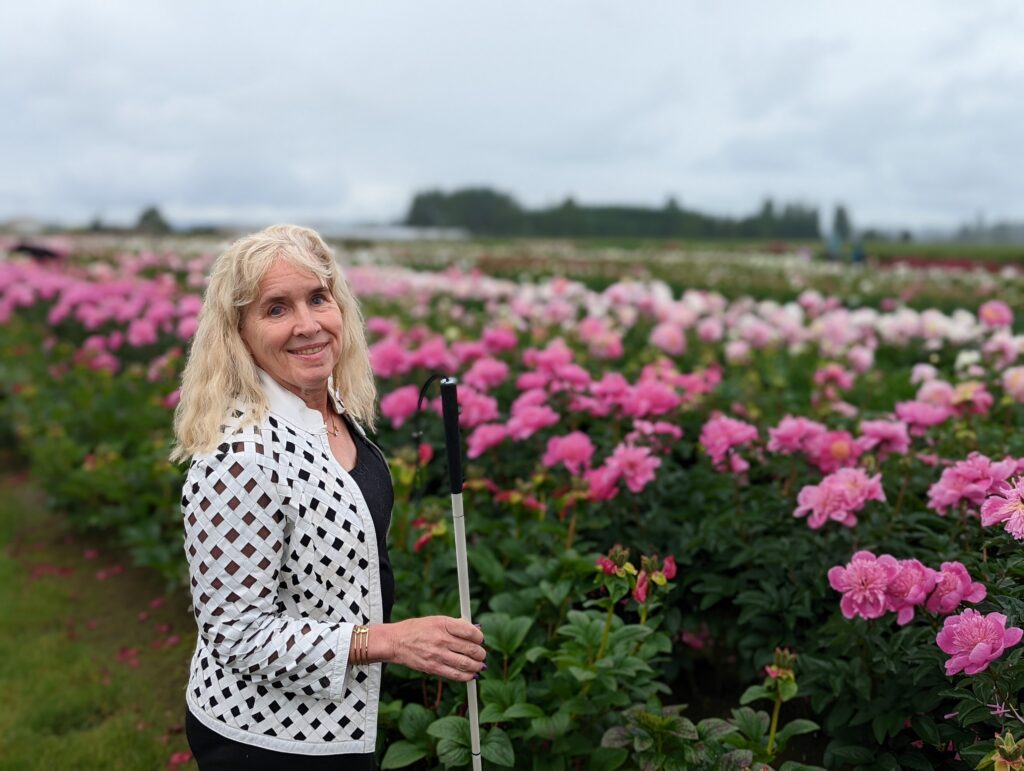 image of Gena holding cane in front of a field of pink flowers