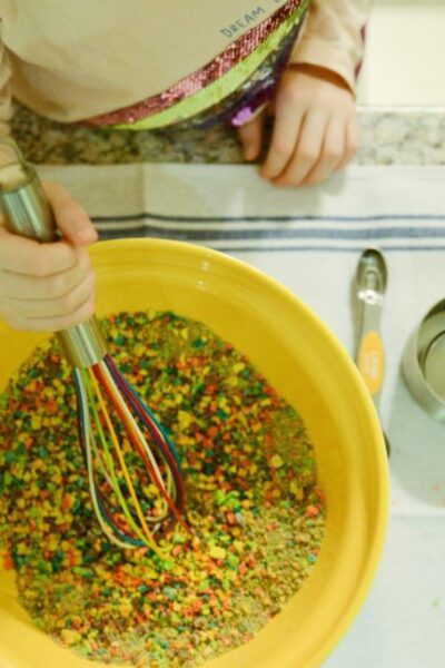 image of a child using a whisk to stir a bowl of brightly colored pulverized cereal.