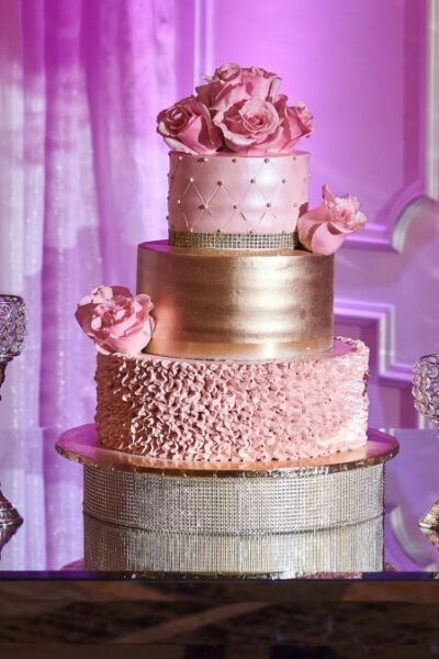 Elegant quinceanera cake on a glass table surrounded by big flower arrangements