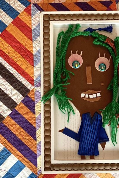 multi-textured, collage self-portrait with cardstock face, wooden eyes, leather lips, ribbon nose, and braided yarn hair