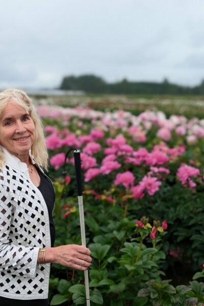 Gena Harper holding a white cane in front of a field of flowers