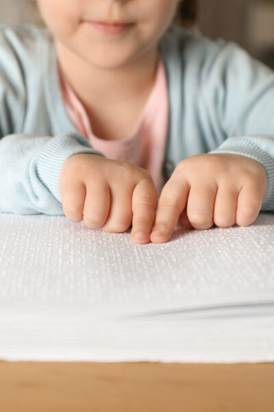 Blind child reading book written in Braille at table, closeup.