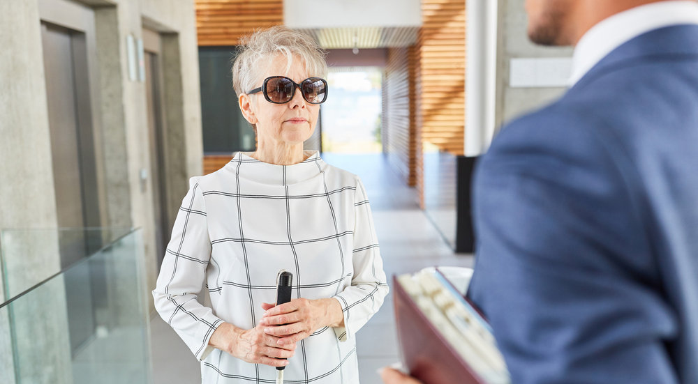 Blind woman with cane in business office talks to a businessman