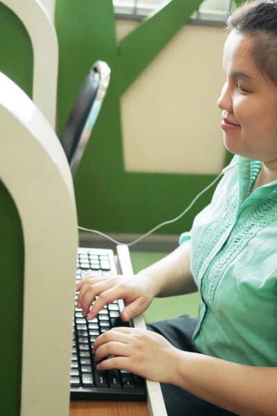 happy woman in headphone typing on computer keyboard working in workplace office.