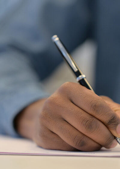 Hands of African American Man Writing on Paper with Pen, Close Up