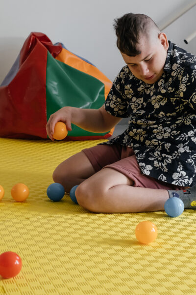 A boy sitting on a sensory mat playing with various balls.