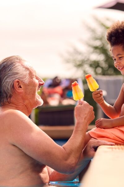 Grandparent and grandchild eat popsicles in the pool