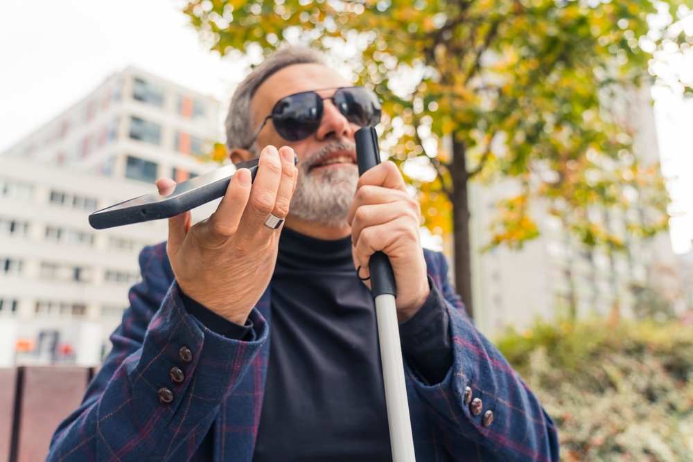 Person with graying hair uses a white cane and smartphone