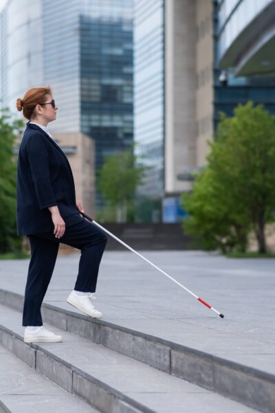 Person wearing business attire walks up office steps with a white cane