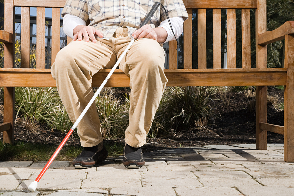 Person sitting on bench holding a white cane