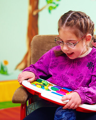 girl in wheelchair playing with developing toy in kindergarten for children with special needs