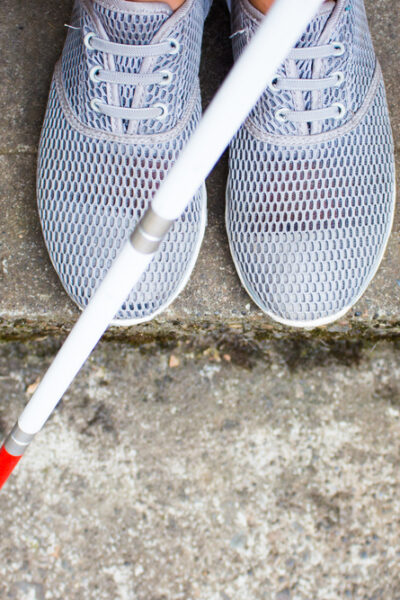 close up of tennis shoes and a white cane