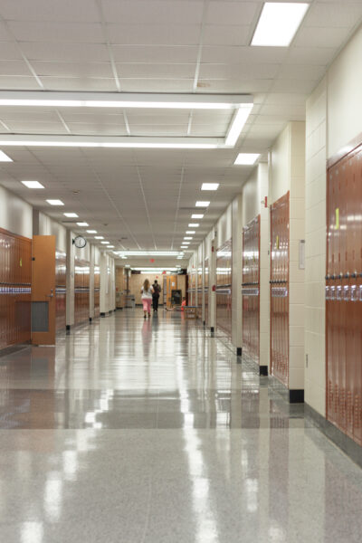 School hallway with lockers with students at the end of the hallway.