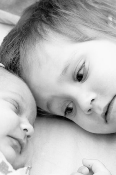 Toddler boy and his newborn sister are lying on a bed. Black and white photo.
