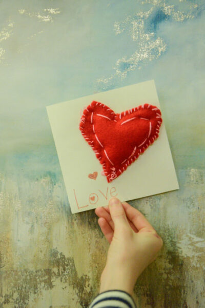 Woman's hand holding a card with sewn felt heart attached.